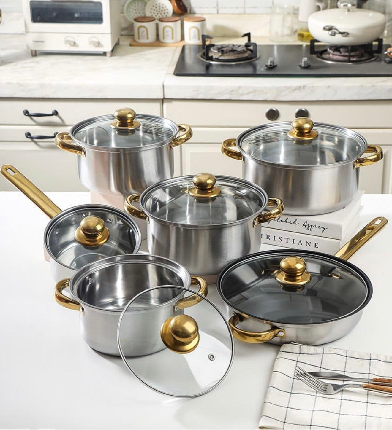 Set of stainless steel cookware with gold handles on a kitchen counter.