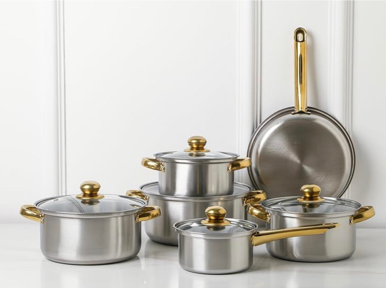 Set of stainless steel cookware with gold handles on a white surface.