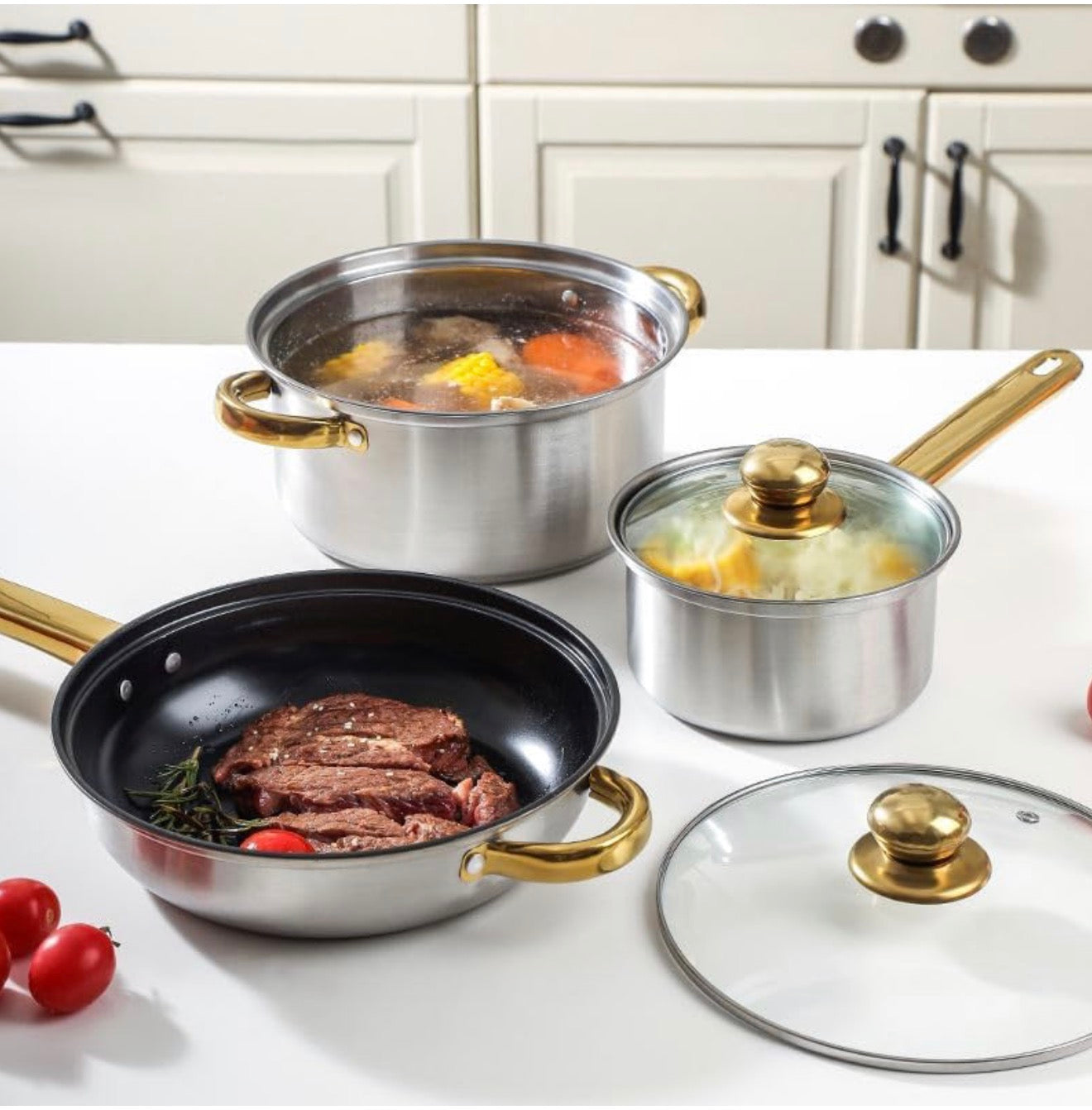 Set of stainless steel cookware with gold handles on a kitchen counter.